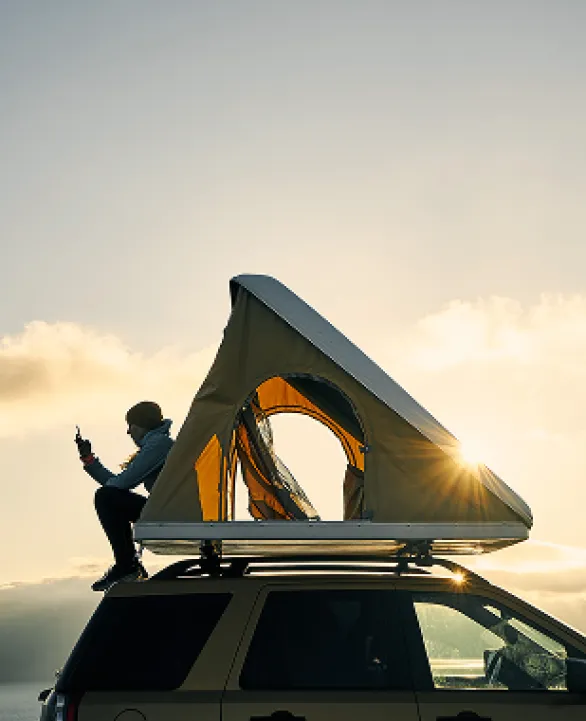 Person sitting on car with roof tent at dusk