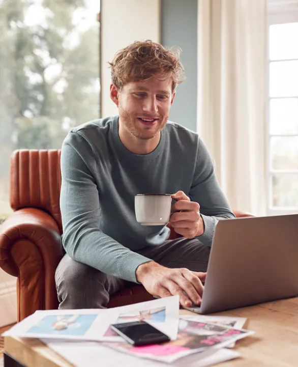 Man sitting down looking at laptop with drink in his hand