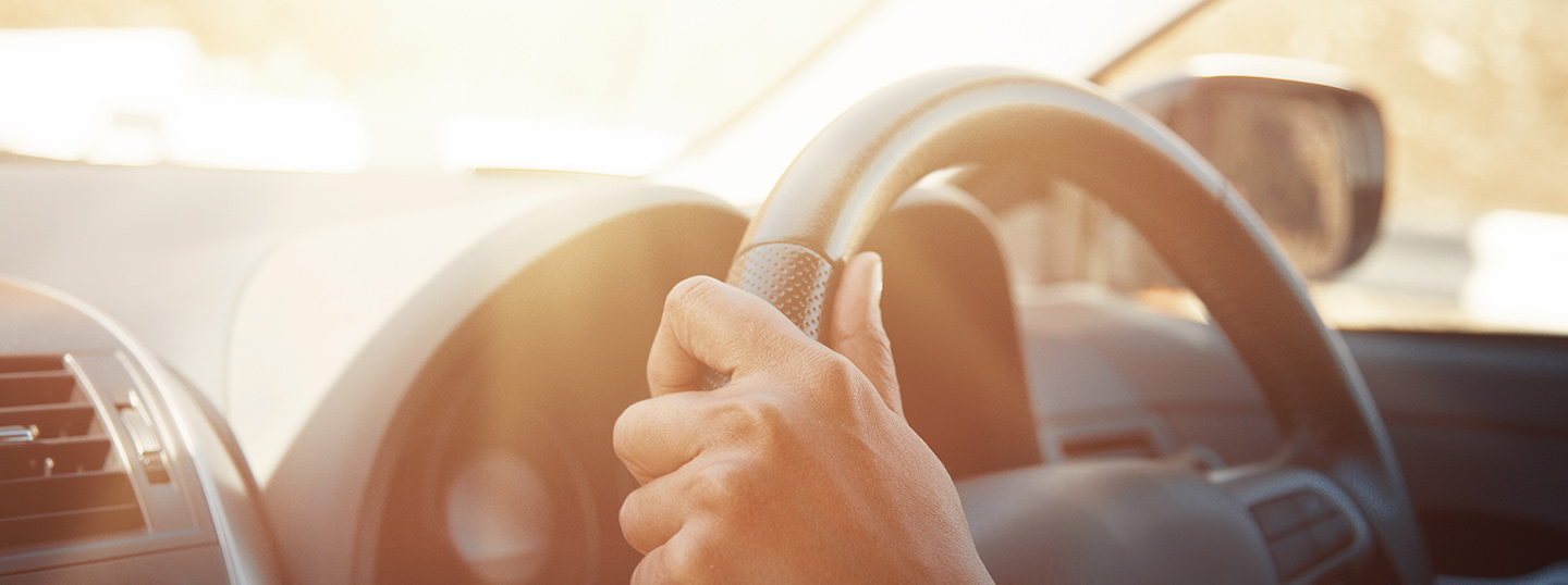 Close up of hands on a steering wheel in the sun