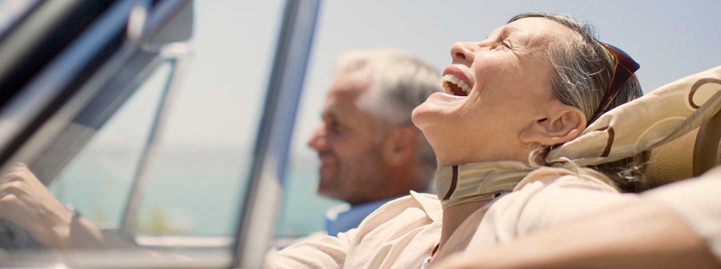 Older couple laughing whilst driving in a convertible in the sun