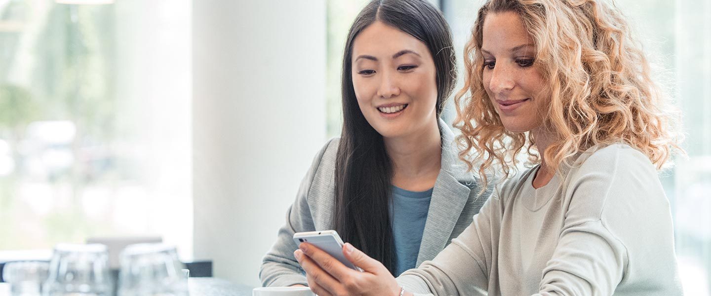 Two women looking at phone in cafe