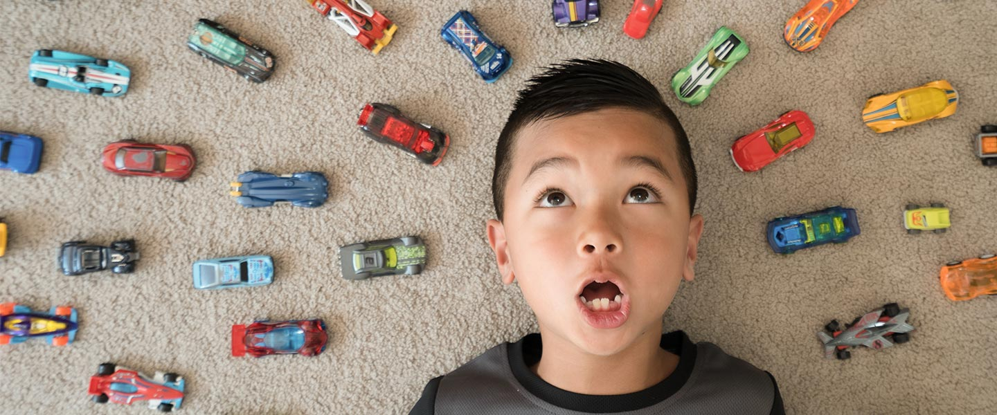 Boy lying on floor surrounded by toy cars