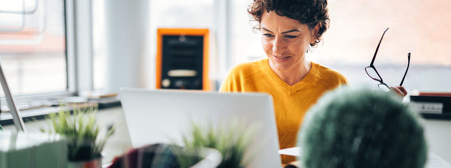 A person with curly brown hair and a yellow jumper happily working at a laptop