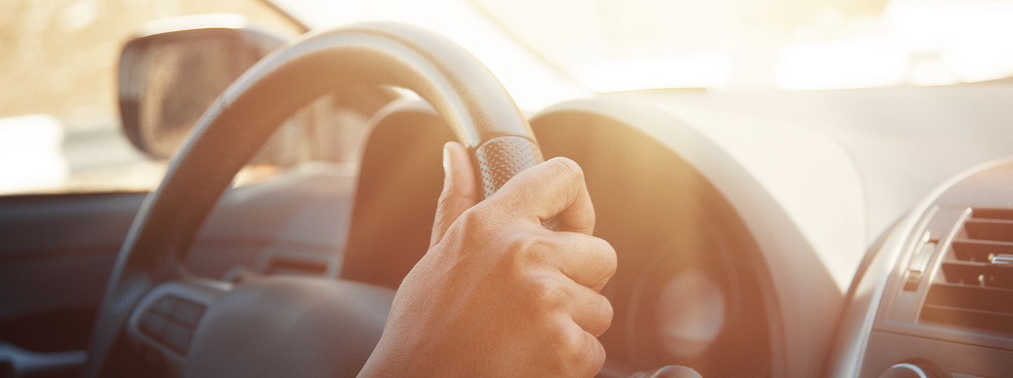 close up of a hand on the steering wheel, the image hazy with glare from the sunset