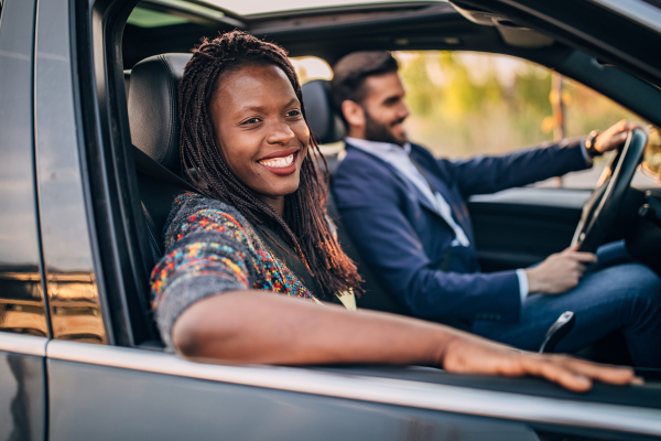 A happy, smiling Black woman looking out of the window in the passenger seat while a man drives